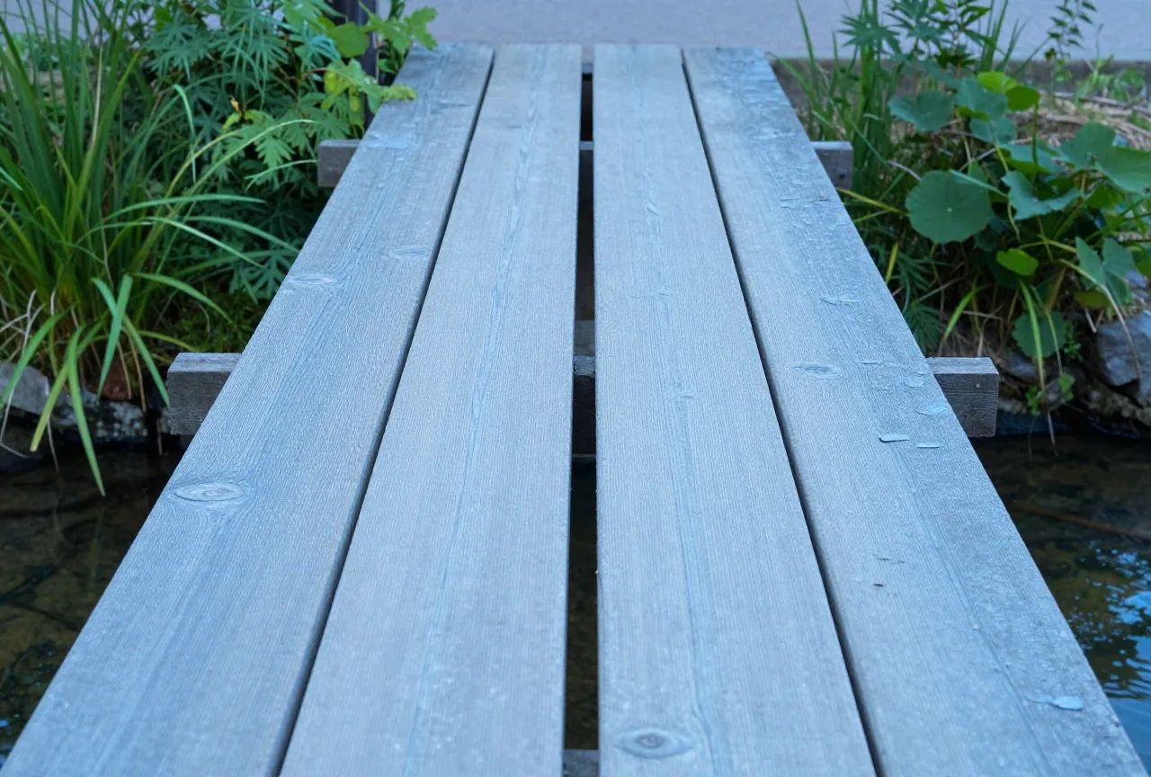 Eine schmale Lücke zwischen zwei Holzbohlen einer kleinen Gartenbrücke über einem Bach