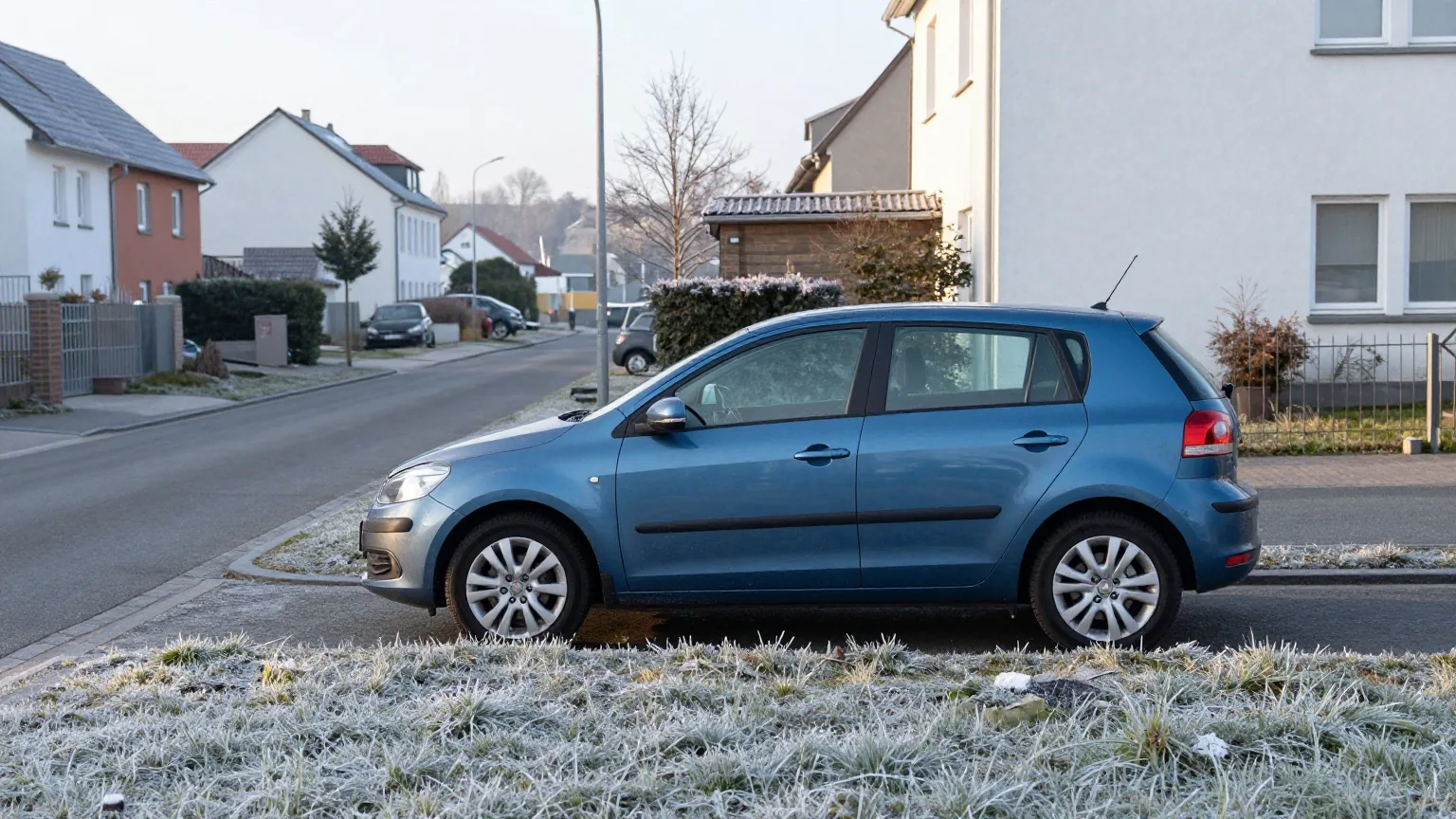 Ein Kleinwagen parkt an einem klaren Wintermorgen in einer ruhigen Wohnstraße, Raureif liegt auf dem Grünstreifen